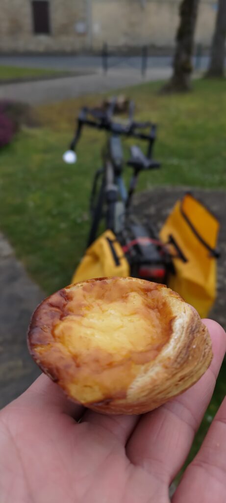 Une pâtisserie Pasteis de Nata tenue dans une main à plat, en arrière plan un vélo