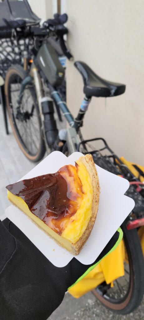 Une main tendue tient une part de flan, un vélo en arrière plan