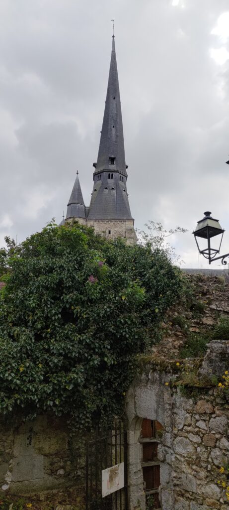 Clocher de l'église de Gallardon vue depuis un petit chemin, masquée par un muret, une petite porte en grille en fer