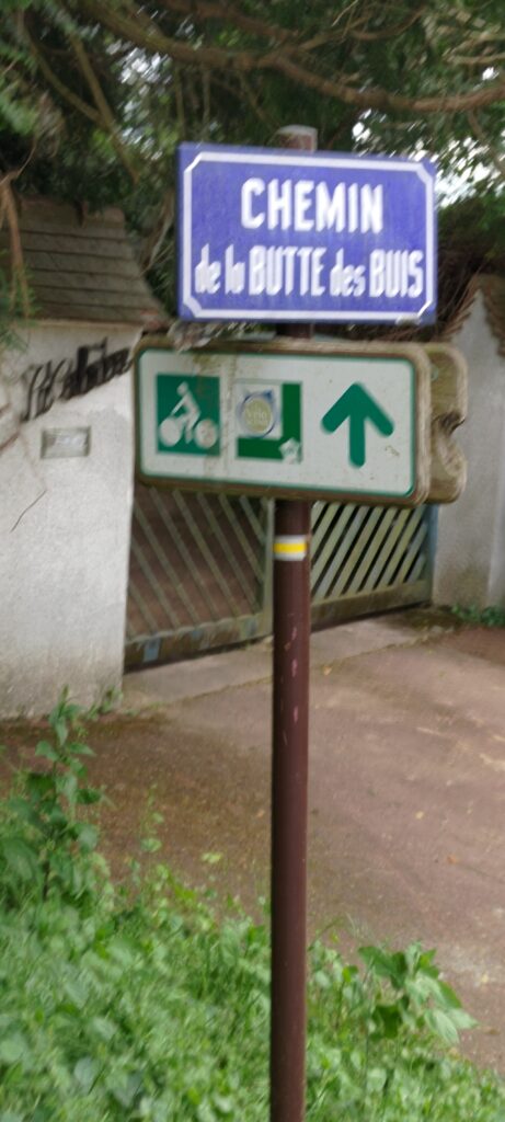 Photo floue d'un panneau de rue "Chemin de la Butte des Buis" et un panneau de voie cyclable "La Véloscénie"