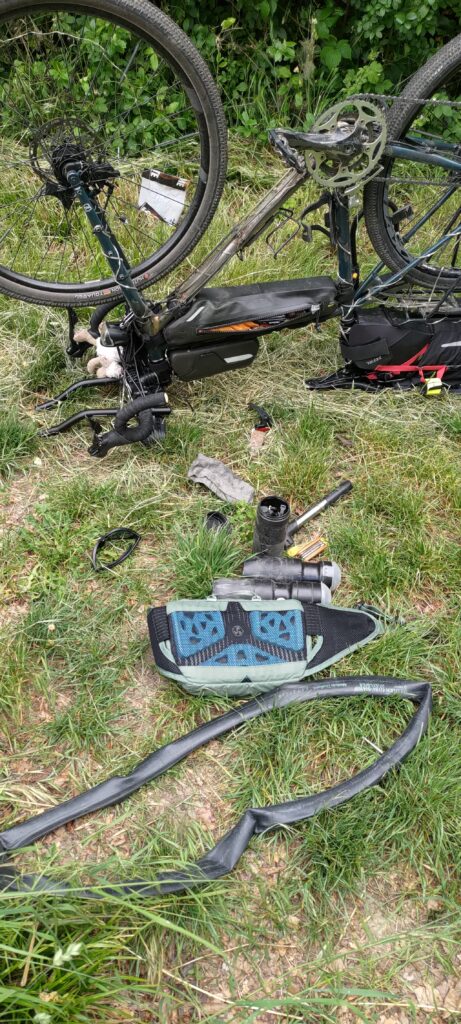 Un vélo retourné posé à l'envers, différents outils posé au sol dans l'herbe dont une chambre à air