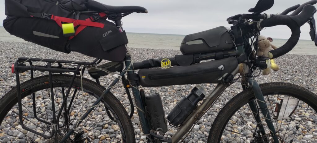 Un vélo vu en gros plan sur une plage de galets. En arrière plan la mer. Posée sur le vélo, une médaille "200"