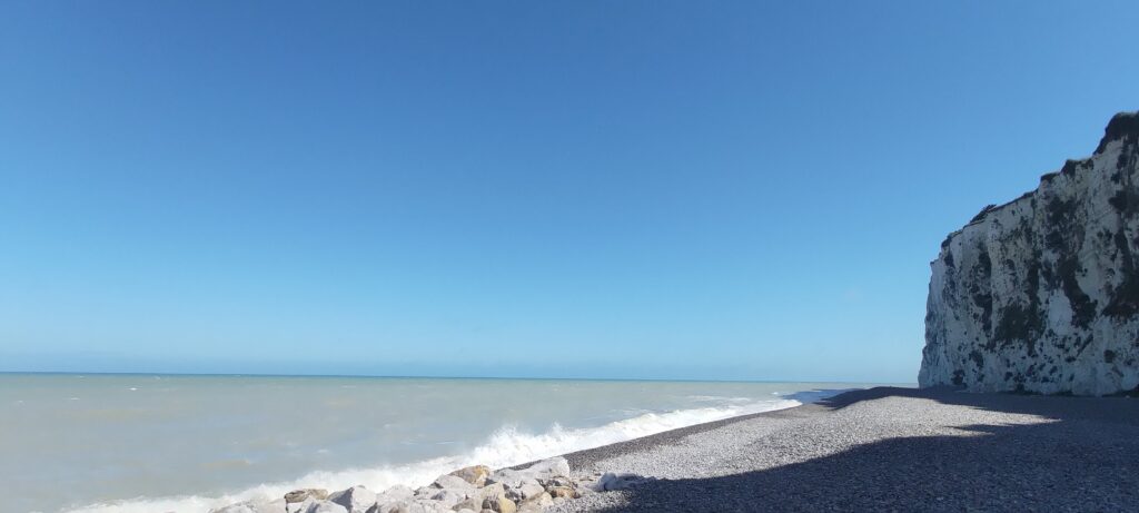 mer grise, ciel très bleu, plage de galets et falaise blanche