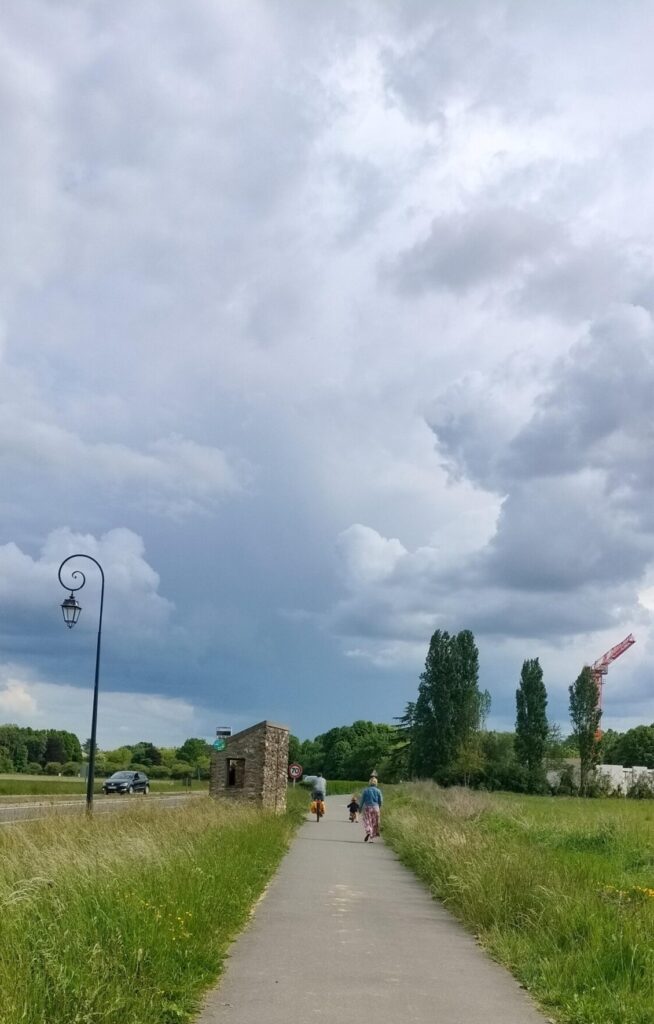 Sur une piste cyclable, une personne adulte sur un vélo, à ses côté un jeune enfant sur un vélo et un peu en arrière une personne adulte à pied. Tous sont de dos et assez éloignés de l'appareil phot.