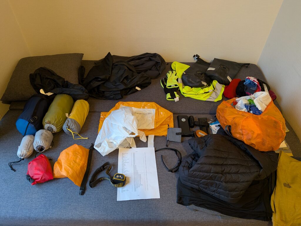Tas de vêtements et d'equipements cyclistes et bivouac posés sur un lit en vrac