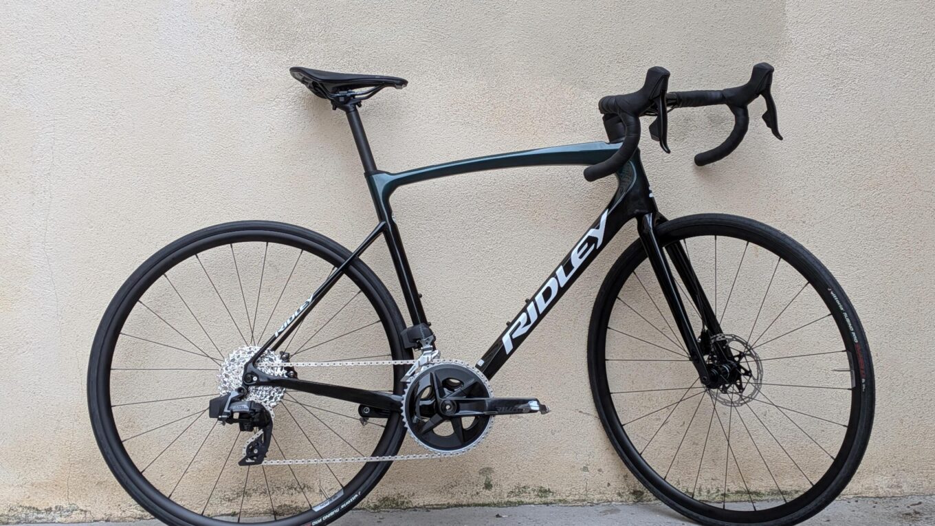 Un vélo type course de couleur foncée posé sur un mur en crépis blanc