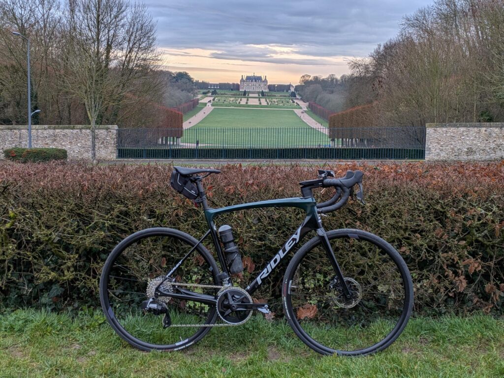 Un vélo de course posé sur un buisson, à l'arrière plan la perspective sur le château de Sceaux