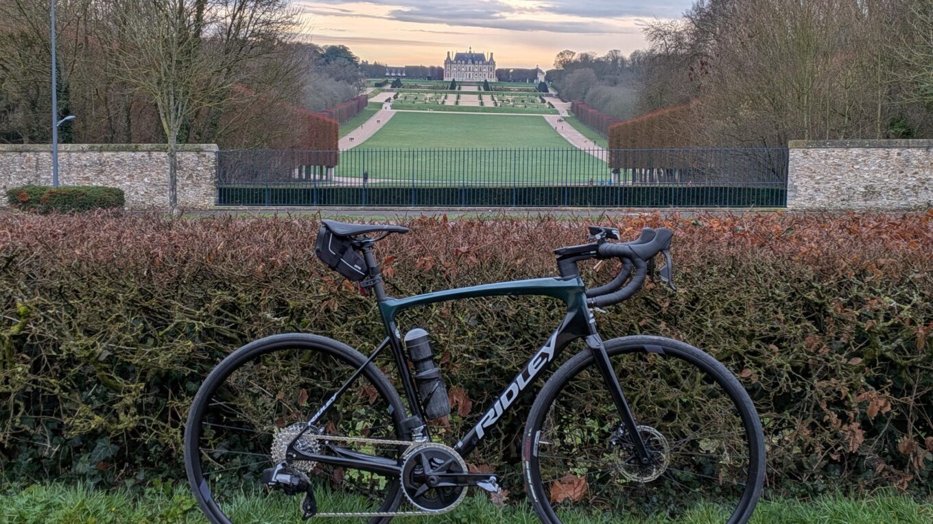 Un vélo de course posé sur un buisson, à l'arrière plan la perspective sur le château de Sceaux