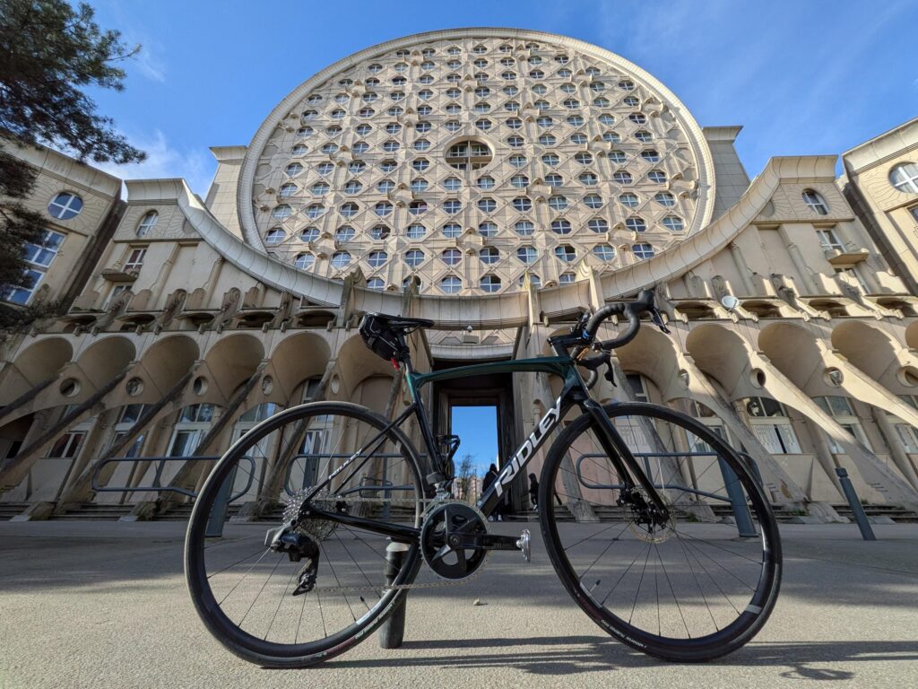 vue en contre plongé au grand angle d'un vélo de course posé devant un immeuble de 14 étages en forme de très grand disque