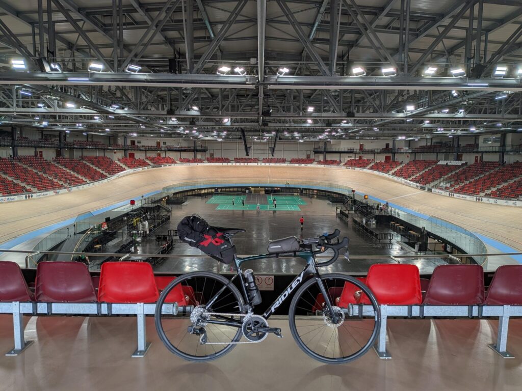 Dans très grand vélodrome, au premier plan un vélo de route et à l'arrière plan la salle immense et la piste en bois