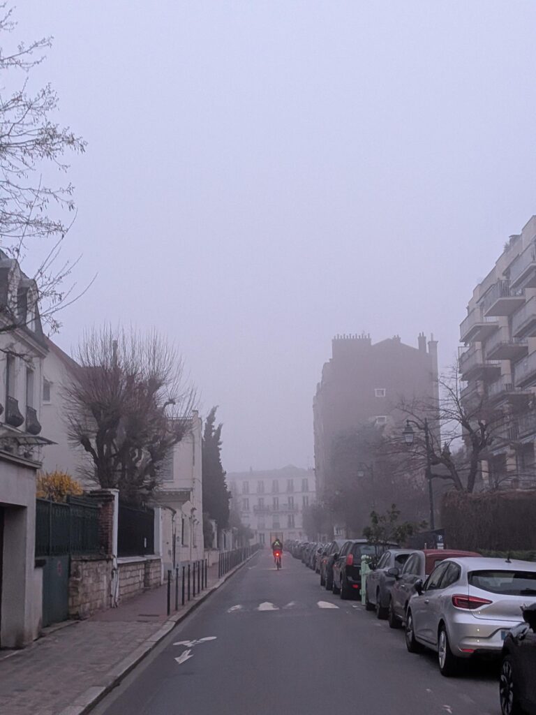Dans une petite rue de banlieue parisienne, un cycliste seul s'enfonce dans la brume