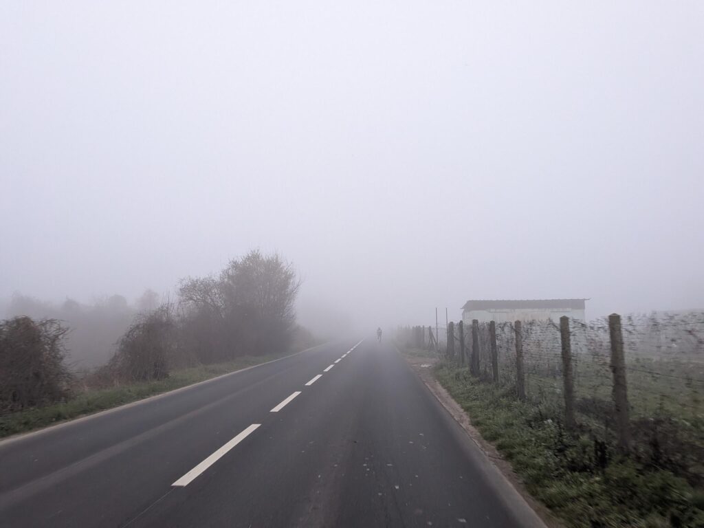 Route de campagne dans la brume, au loin un cycliste