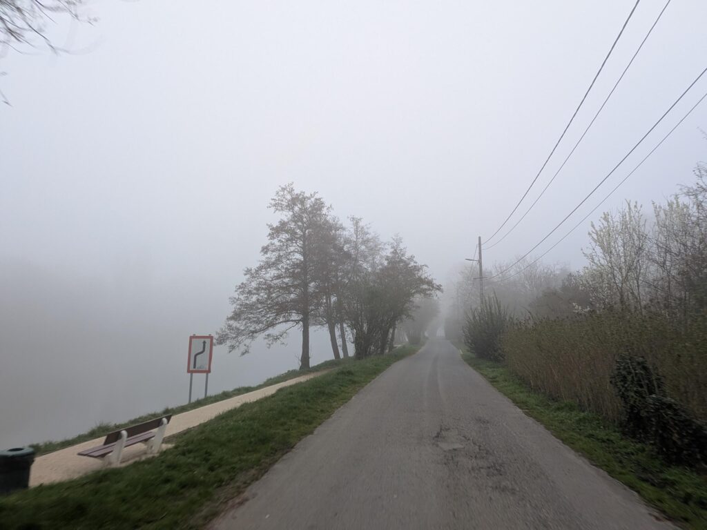 Une route au bord d'un fleuve que l'on ne voit pas à cause de la brume