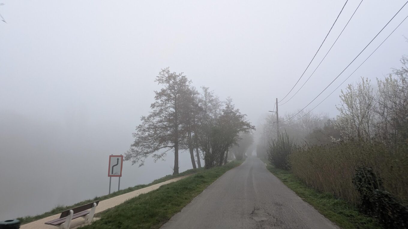Une route au bord d'un fleuve que l'on ne voit pas à cause de la brume