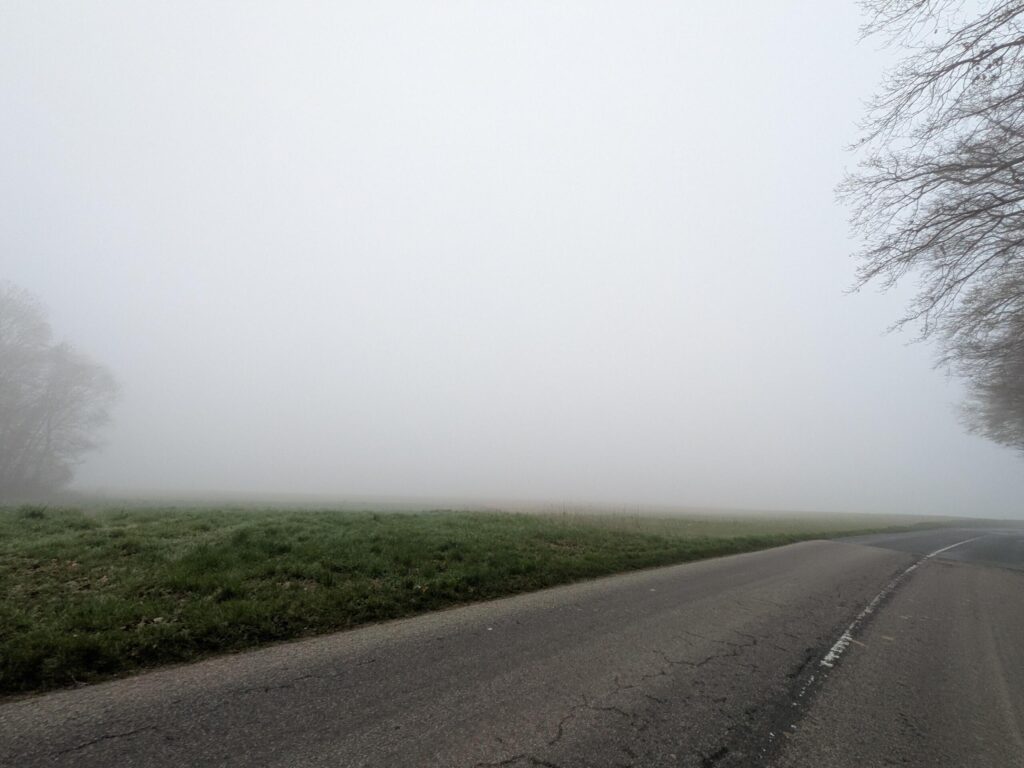 une route de campagne qui tourne, on devrait voir un paysage car on est au sommet d'une colline mais juste de la brume