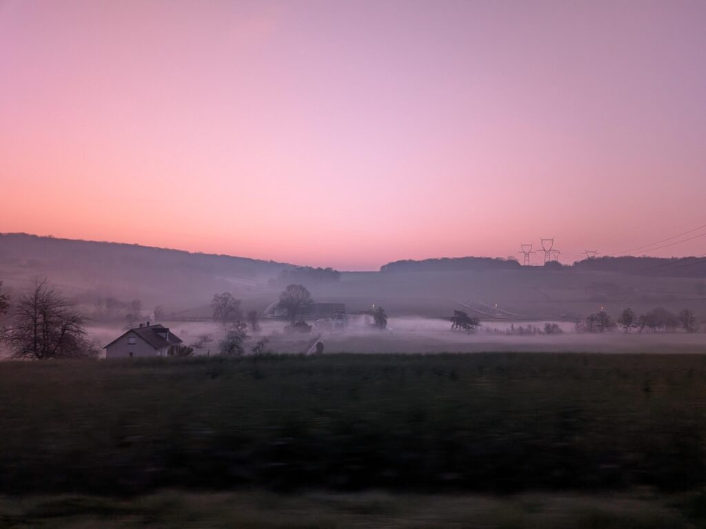 Au petit matin, un ciel rose, paysage de campagne avec une brume qui est très présente et concentrée dans la vallée