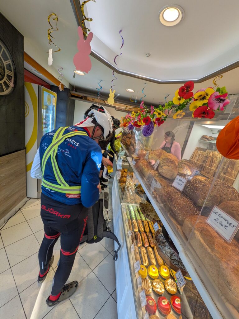 Dans une boulangerie, plusieurs cyclistes de dos font la queue