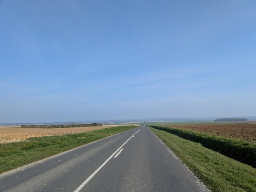 À la campagne, une route type départementale en ligne droite en pente, personne dessus, des champs autour