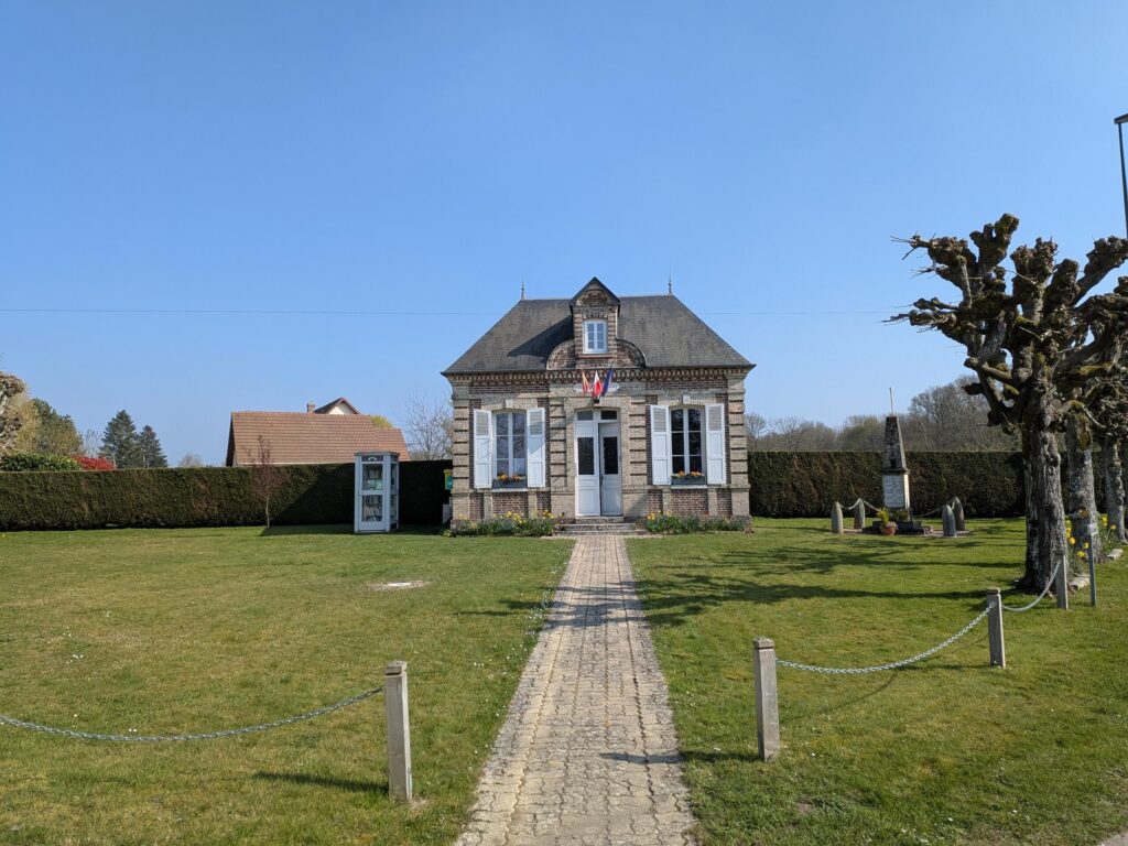 Une toute petite mairie devant une grande pelouse et de part et d'autre une cabine téléphonique convertie en boite à livres et un monument aux morts