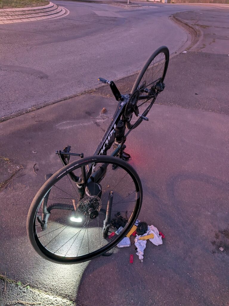 De nuit un vélo retournée, la roue avant démontée et des outils au sol