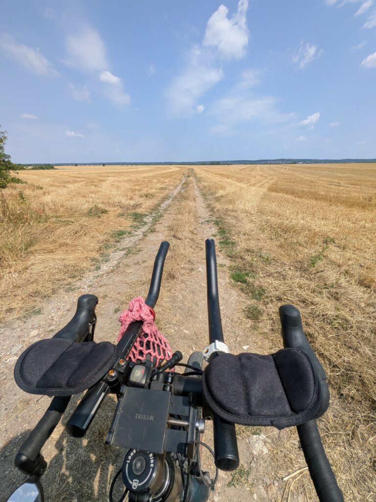 vu subjective d'un cycliste sur un petit chemin au milieu de champs jaunis par le soleil