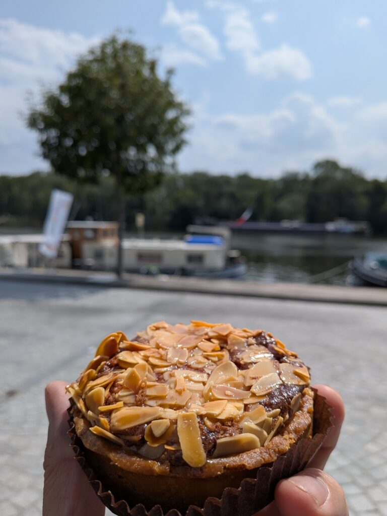 Une main tient une pâtisserie, en arrière plan flou une rivière
