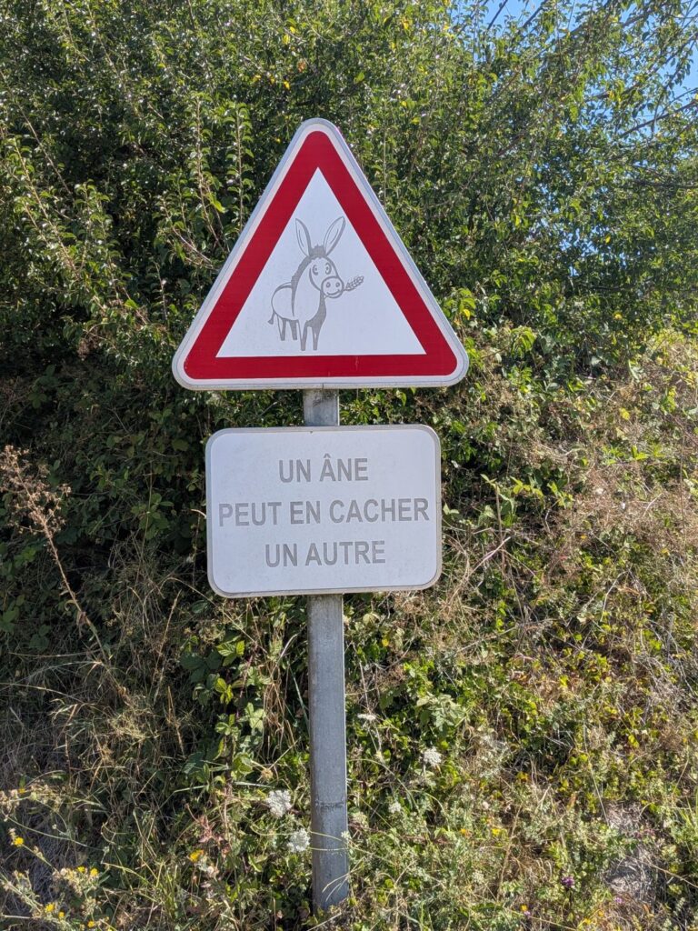 Panneau de circulation triangulaire avec un âne et texte "Un âne peut en cacher un autre"