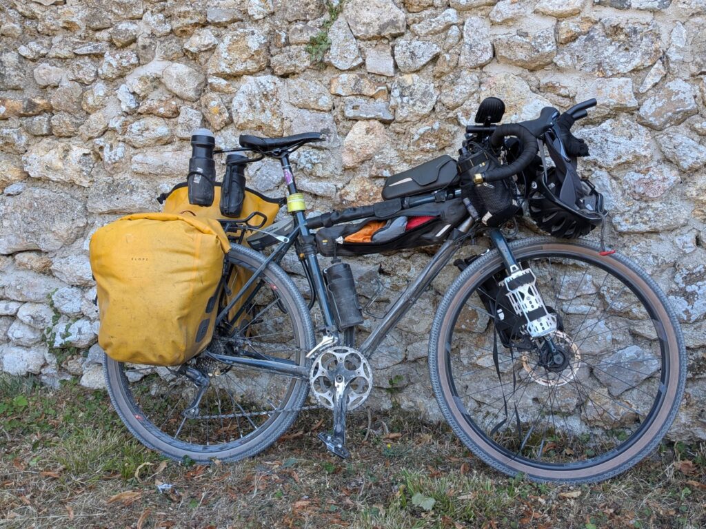 un vélo type gravel avec sacoches et équipements de voyage posé sur un mur en pierres claires