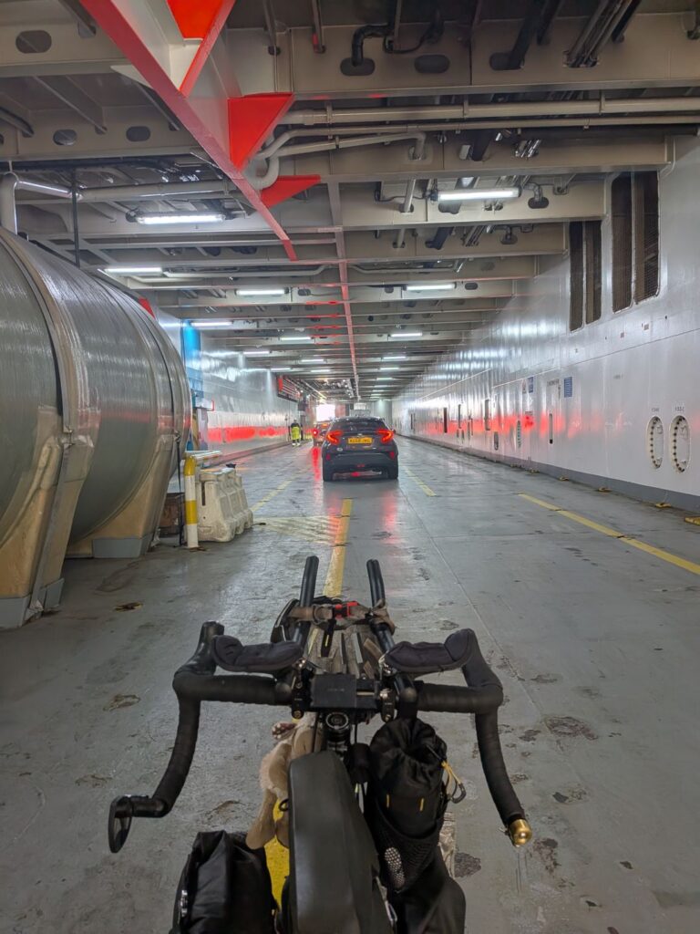Dans la soute d'un ferry, vue subjective d'un cycliste montrant son vélo et faisant la queue avec les voitures