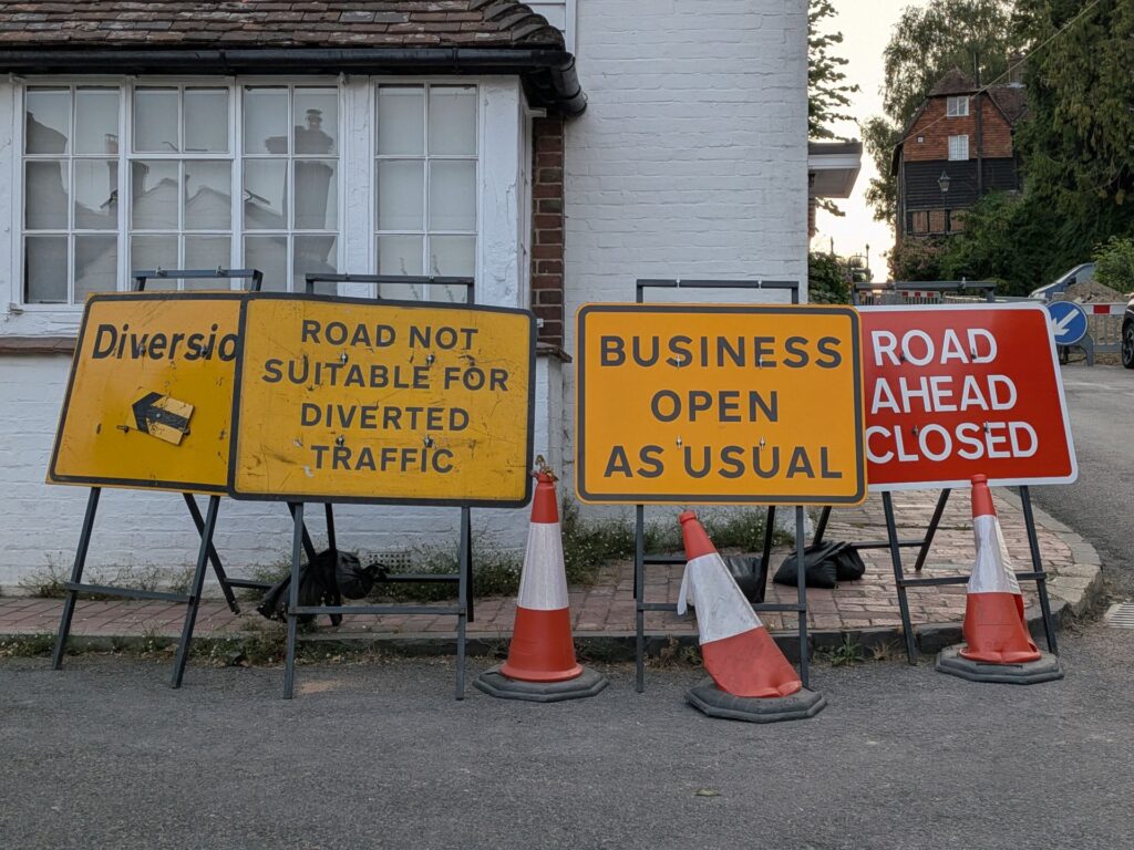 Plusieurs panneaux en anglais indiquant un chantier, fermeture de route, déviation et commerces toujours ouverts
