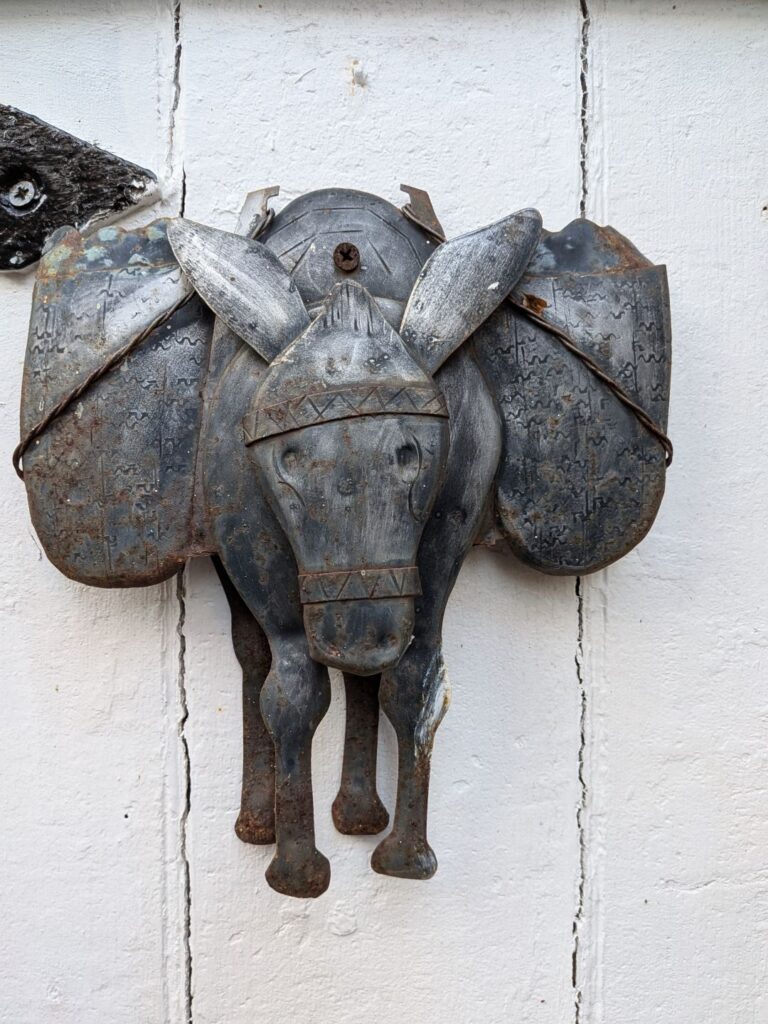 Gros plan sur une sculpture d'âne portant des charges de chaque côté, réalisé en métal et posé sur une porte en bois blanche