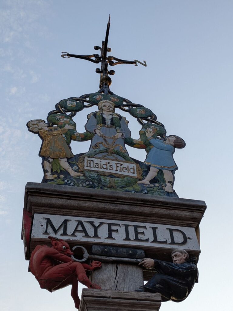 Poteau ornée de décoration dont le nom de la ville de Mayfield et notamment un diable et un curée qui se disputent une clé
