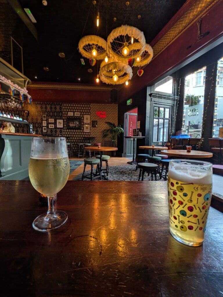 Deux verres de bière sur une table d'un bar, reflet d'un lustre sur la table et lustre visible également sur la photo
