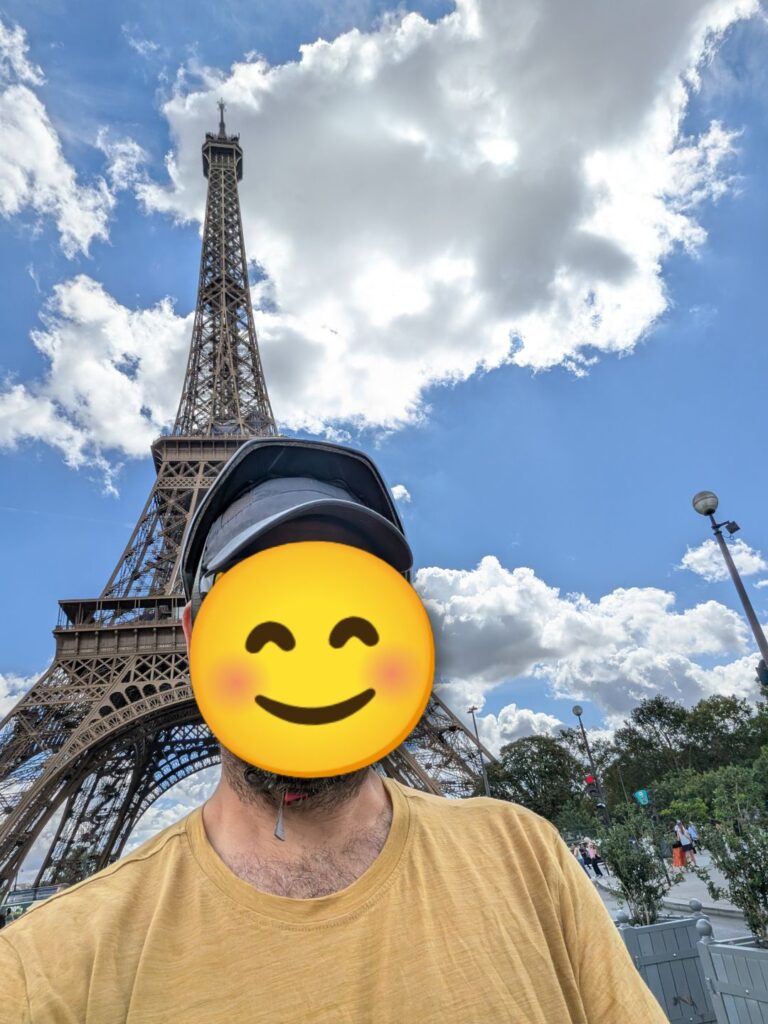 Autoportrait d'une personne dont le visage est masqué par un smiley, derrière la tour Eiffel