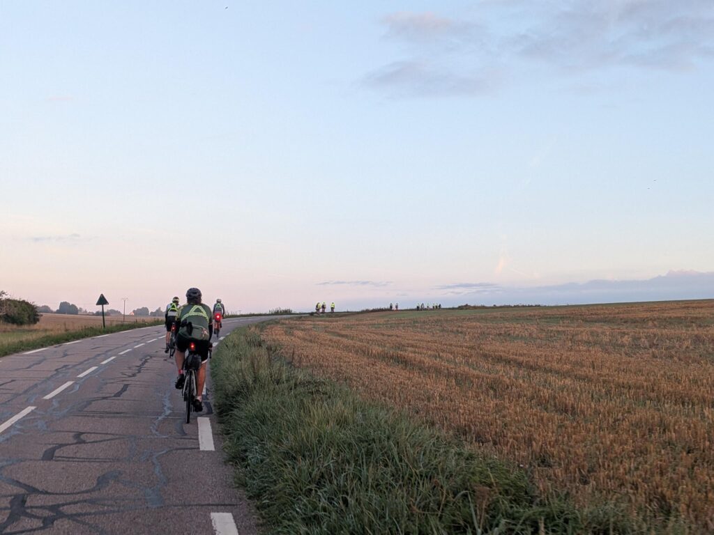 au petit matin, soleil levant dans le dos, sur une route en courbe et montante, plein de cyclistes