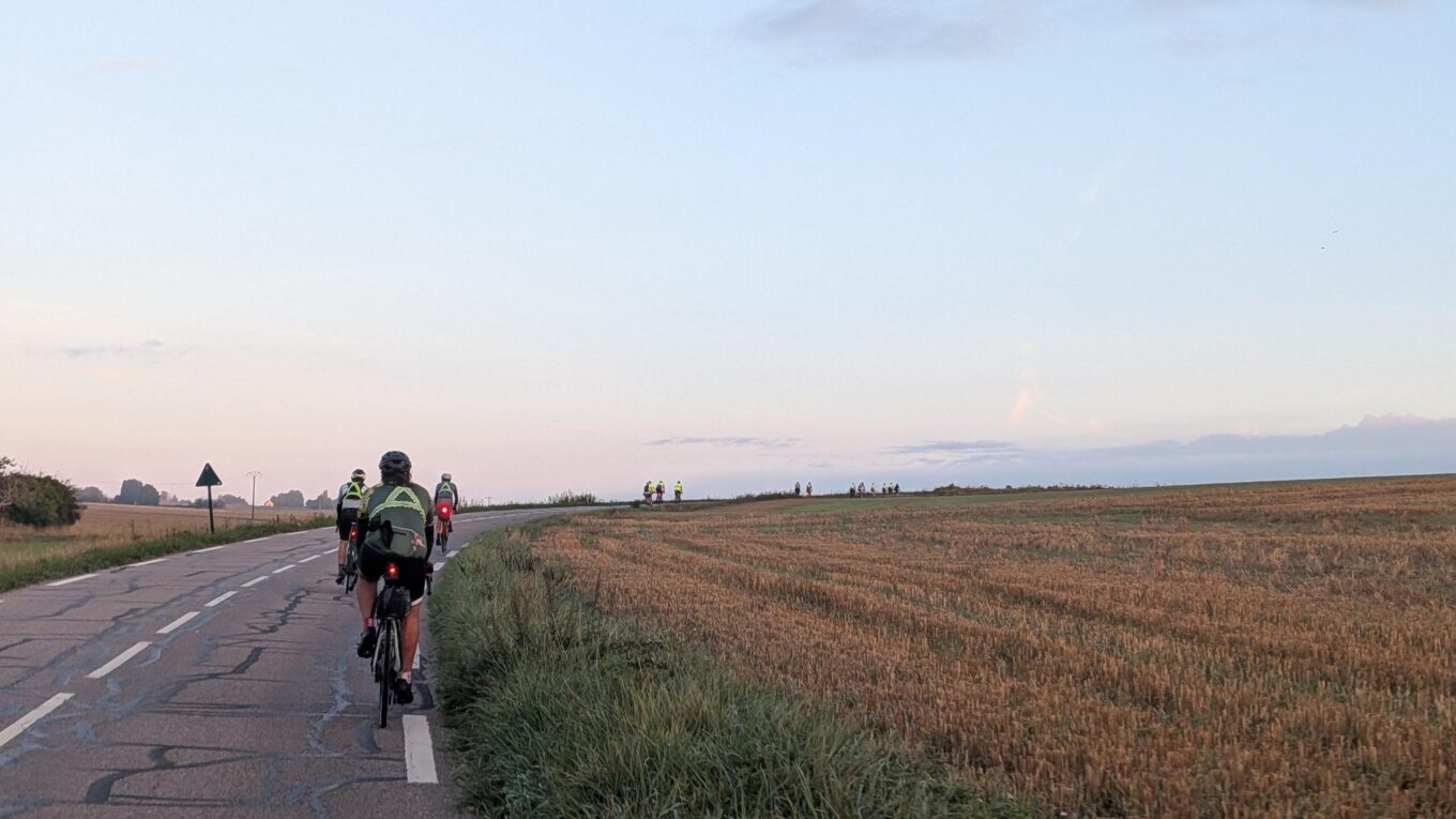 au petit matin, soleil levant dans le dos, sur une route en courbe et montante, plein de cyclistes