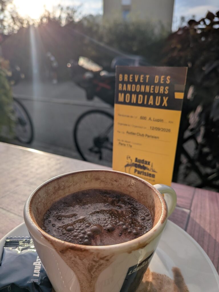 Une tasse de chocolat en terrasse et un papier jaune Brevet des randonneurs mondiaux