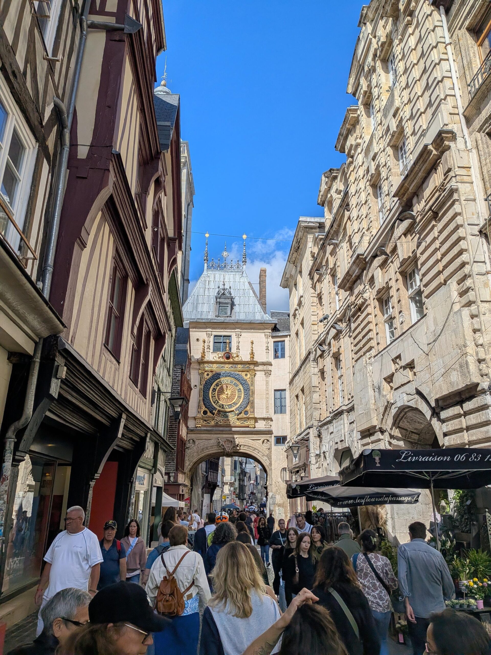 Petite rue très fréquentée par des piétons qui passent sous un immeuble décoré d'une très grande horloge dorée