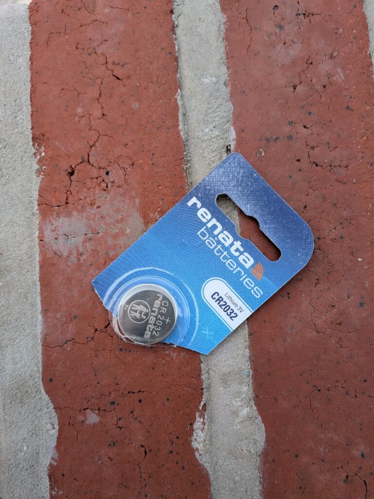 Un sachet de pile bouton neuf ouvert posé sur un sol en briques