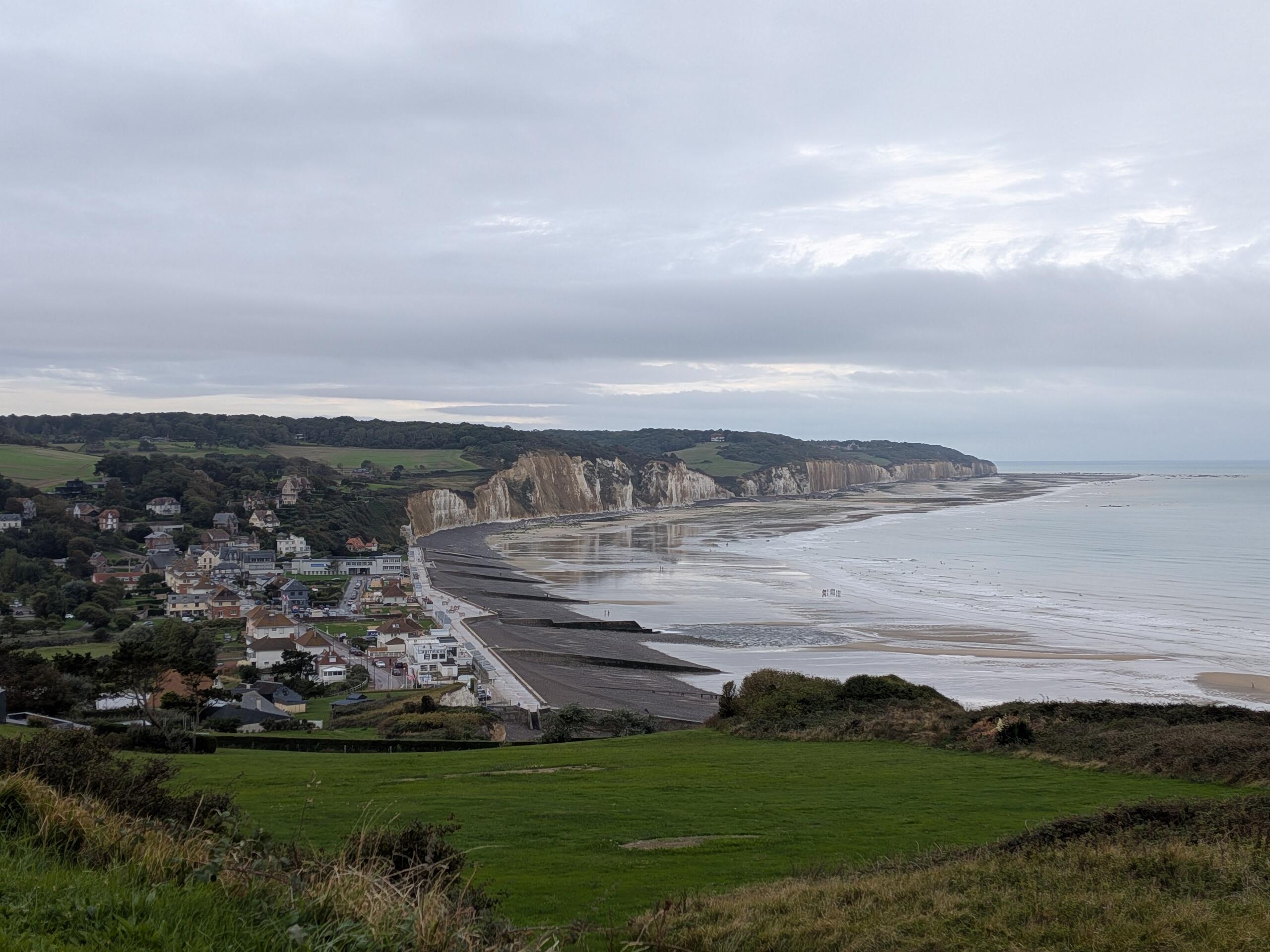 Paysage de falaise typique de la Normandie, à gauche une petite ville de bord de mer, au milieu la plage, à droite la mer et au fond les falaises