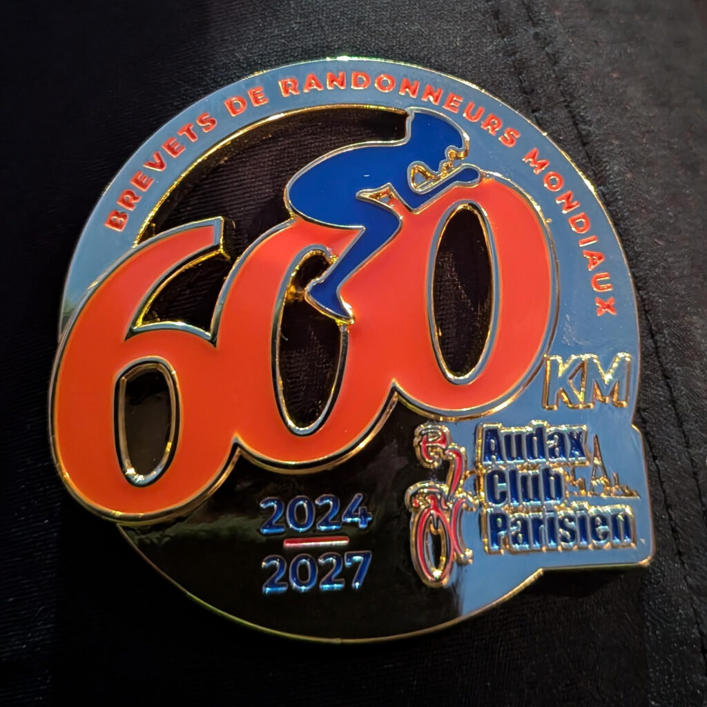 Médaille avec un gros 600 et une personne dessus comme sur un vélo. Brevets de randonneurs mondiaux 2024/2027